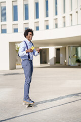 Fototapeta premium Black businessman on a skateboard holding a smartphone outdoors.