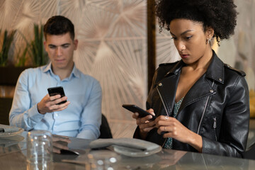 Young couple bored sitting at restaurant distracted by smartphone screen. People always connected to the internet addicted by technology concept.