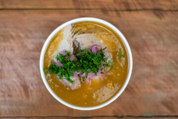 plate of traditional fish soup from the Ecuadorian coast, zenithal view, encebollado, on a wooden table.