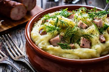 Potato puree - mashed potatoes with sausages and dill in bowl on wooden table