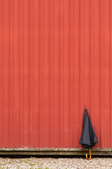 Black umbrella leaning  up against a red metal building