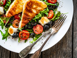 Fresh vegetable salad with grilled halloumi cheese, tomatoes,  lettuce, green leaves, black olives and onion on wooden table
