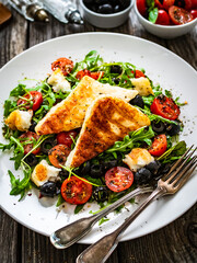 Fresh vegetable salad with grilled halloumi cheese, tomatoes,  lettuce, green leaves, black olives and onion on wooden table

