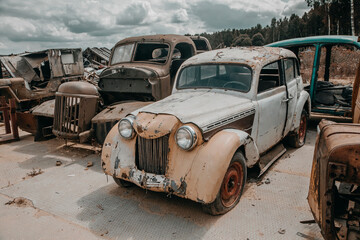 Obraz na płótnie Canvas Old rusty car in the abandoned car graveyard. Old shabby rusty car. Car graveyard.