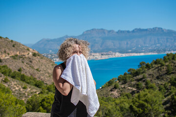 Naklejka premium Blond woman wiping sweat on a towel after running on a sunny day