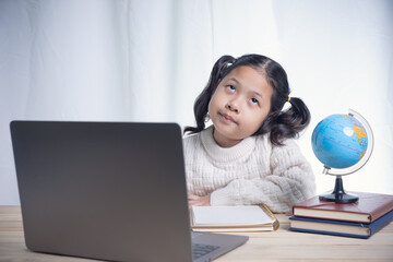 Asian kid girl writing follows teacher for learning an online lesson by video call the Internet...