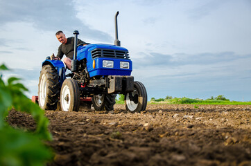 A farmer on a tractor works the field. Milling soil, crushing and loosening ground before cutting rows. Land cultivation. Farming, agriculture. Preparatory earthworks before planting a new crop.