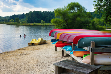 A summer lakeside beach with people playing in the water with colorful canoe racks nearby.
