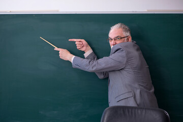 Old male teacher in front of blackboard