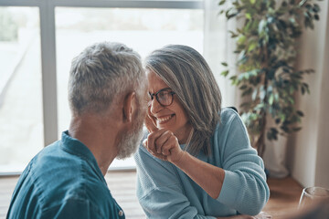 Playful senior couple sitting face to face and smiling while spending time at home
