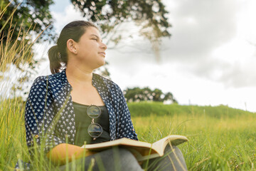 Hermosa mujer caucásica leyendo un libro en una zona verde a la orilla de un lago