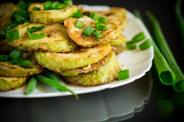 fried zucchini in circles with fresh herbs in a plate on a black