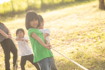 Fototapeta premium Children playing tug of war at the park on sunsut