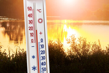 Thermometer on the background of the river at sunset shows 20 degrees of heat. Summer and autumn temperatures in the evening