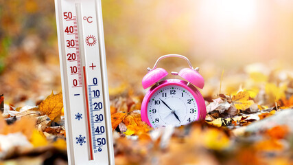 Thermometer in the autumn forest near the clock on a background of yellow fallen leaves shows 15...