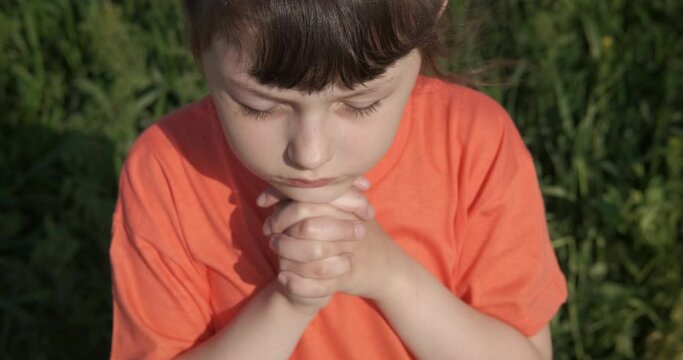 Make a wish in the field. A little happy child feen the wind and pray in the green grass in the meadow.