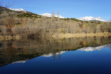 mirror reflection of the mountains with snowy peaks in the water on a clear winter day in the alps, france