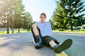 Fashion portrait of hipster teenager guy sitting on the road.