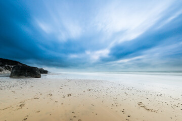 Long exposure photo of clouds rolling over a sand beach.