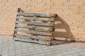 a pallet leaning against a wall casting its shadow