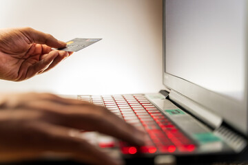 Selective focus of a mann hand holding credit debit card while type payment information on laptop or c omputer for online purchase from home. Technology and Social distance concept