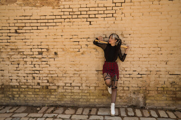 Pretty young girl with heterochromia and punk style with a baseball bat back of her head resting on a yellow brick wall in the background looking to the side.