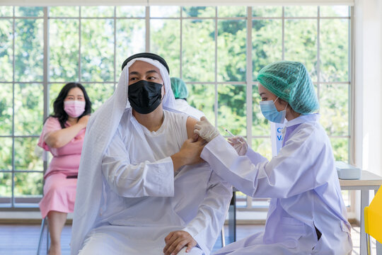 Asian doctor use syringe to injecting covid-19 vaccine into the Arab people in the hospital to prevent outbreak of coronavirus. Immunization, Covid-19 vaccination clinic, Coronavirus global pandemic.