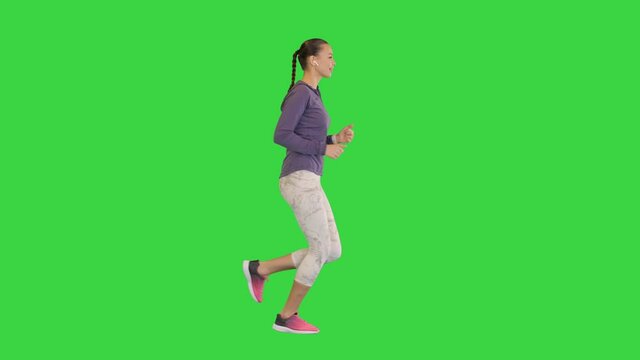 Female runner athlete running and listening music in wireless ear buds on a Green Screen, Chroma Key.