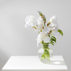 A bouquet of three white irises and a fern in a transparent vase on the table.