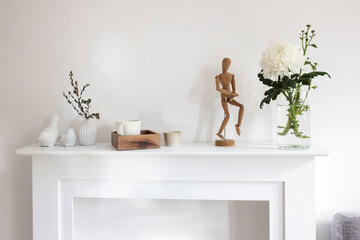 A chrysanthemum in a transparent vase, a cork board with empty leaves, a wooden tray with a cup of coffee, a vase with eucalyptus, a mirror and a figurine of birds. Scandinavian style.
