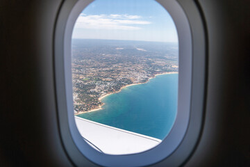 Airplane porthole window with the coast, beach and ocean view from the interior seat. Travel Concept