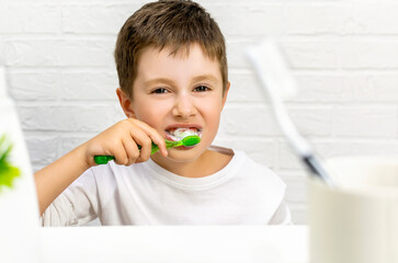 Portrait of happy cute kid boy in white pajamas brushes his teeth with a toothbrush and paste in...