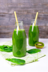 Two bottles of spinach smoothie on a kitchen napkin and green leaves, organic green vegetable and fruit juice in a glass with a straw, a vitamin drink for a healthy diet, diet and slim.