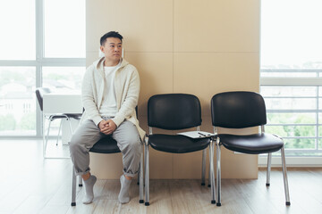 young asian man waiting for an interview or meeting sitting in the hallway in the waiting room....