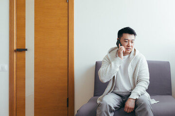 A young man is waiting in the hallway of a clinic or office center, talking on the phone and sharing news and the result of the interview, serious in everyday clothes