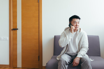 A young man is waiting in the hallway of a clinic or office center, talking on the phone and sharing news and the result of the interview, serious in everyday clothes