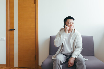 A young man is waiting in the hallway of a clinic or office center, talking on the phone and sharing news and the result of the interview, serious in everyday clothes