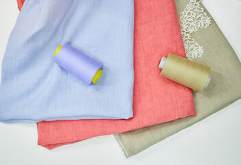 Obraz na płótnie Canvas Cotton linen cloth fabrics in blue, pink and green colors with sewing thread near it. Closeup isolated colorful towels. Sewing items or tailoring objects concept. High quality photo