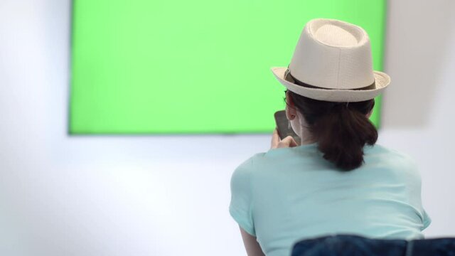 Girl Sits in Font of a Geen Sreen TV and uses phone, Green Chroma Key Screen TV, Relaxing on a Couch