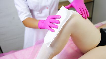 close-up of the hand of a sugar epilation master who applies a napkin to the model's leg.