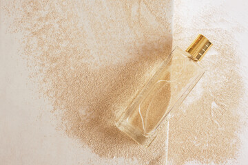 transparent glass perfume bottle with golden cap on sand background