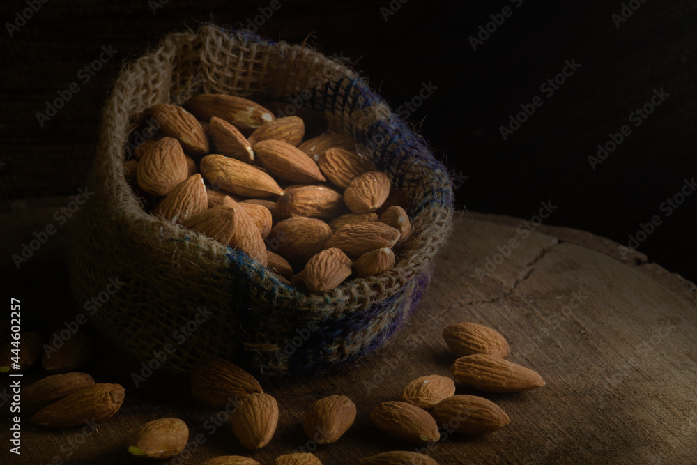 Wall mural Almonds spill out of a rough bag on a black wooden table.