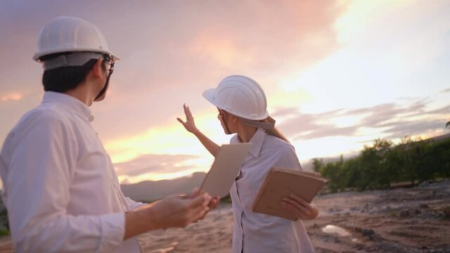Asian Engineer architecture investor wear safety protected hardhat survey at outdoor construction site debriefing work during sunset, specialist expert working field, Real Estate industry innovation