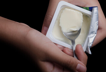 Girl holding a cup of set yoghurt and spoon in hand. Yoghurt is made from milk fermented by added...