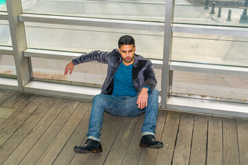 Against a glass wall, a young guy with beard and mustache is sitting on the floor into deeply...