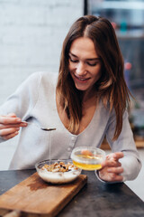 Young woman in the kitchen adds honey to muesli.