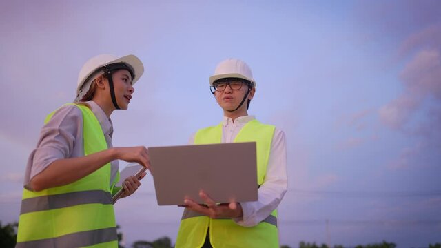 A professional senior constructor giving a job explanation to young trainee on construction site, happy teamwork, young female architect discussing on possible designing as clients required, 