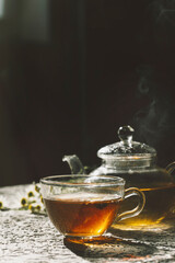 a cup of tea with steam with a glass teapot on a dark background 