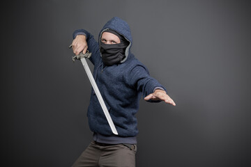 American Brutal man in a blue hoodie and black face mask with a Fantasy Handle Sword. Portrait of a...
