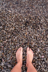 Bare female feet on pebble stones beach, top view